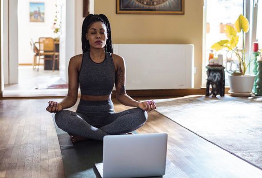 Woman doing yoga meditation at home with laptop